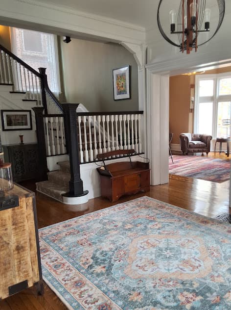 A welcoming entryway features a staircase, a cozy sitting area, and an ornate rug.