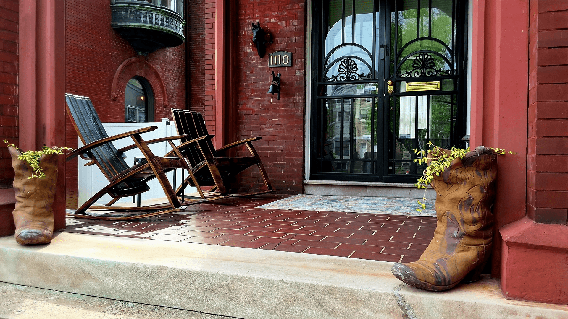 A porch with two rocking chairs and decorative planters shaped like cowboy boots.