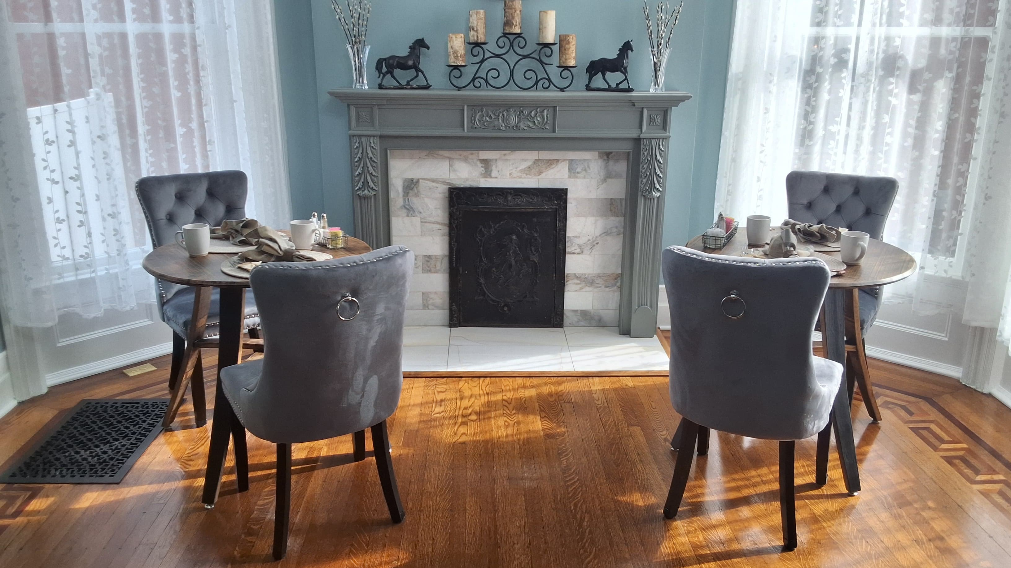 Cozy dining area with two circular tables, gray upholstered chairs, and a decorative fireplace.